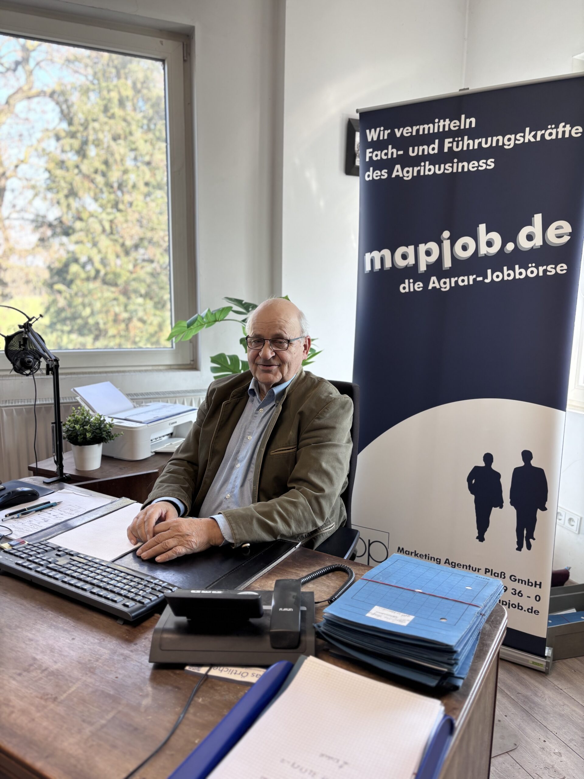 Geschäftsführer Herr Plaß sitzt lächelnd am Schreibtisch in einem hellen Einzelbüro.
